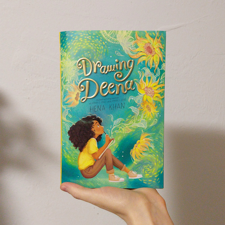 Drawing Deena by Hena Khan. Cover is artwork of a young girl with dark curly hair, sitting with a sketchbook and pencil, wearing a bright yellow shirt. The background is teal with bright yellow flowers and bright swirly yellow and green designs.