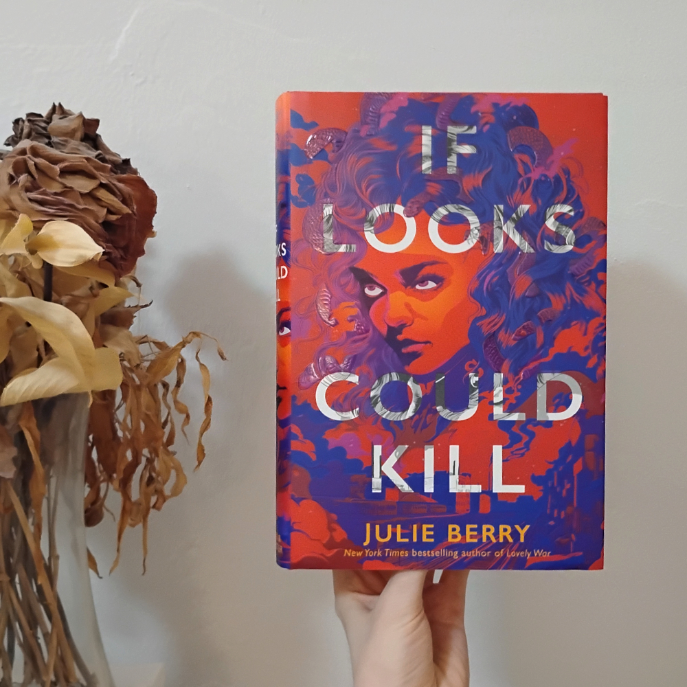 If Looks Could Kill by Julie Berry. The cover is an illustration of a girl's face, all in bold red and purple and orange. She has an intense look and snakes mixed in with her hair. The bottom sorta fades out and turns into a view of a city street.