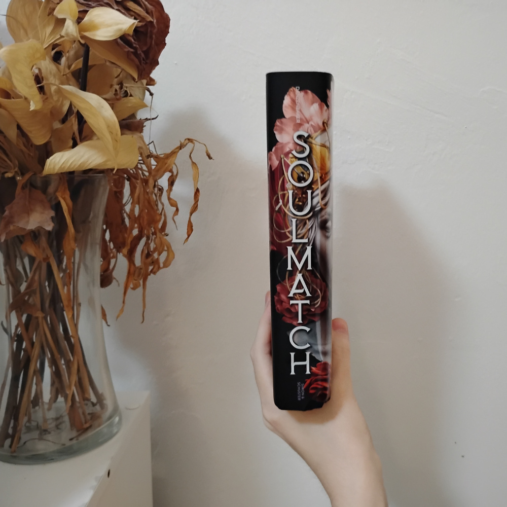 The spine of the book, the face and flowers from the front continue onto the thick spine, so it's mostly red and pink flowers with the title in white text.