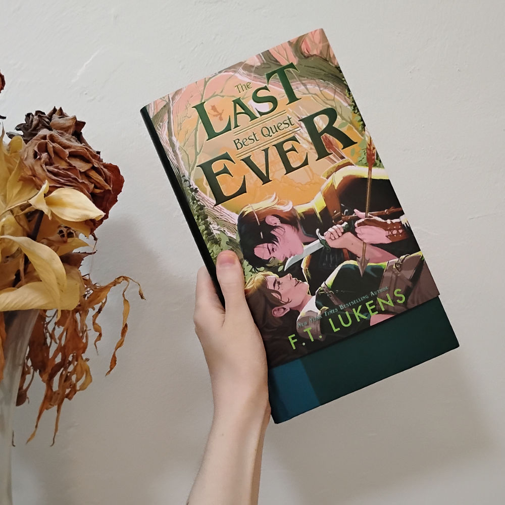 Photo of The Last Best Quest Ever by FT Lukens hardcover with the dust jacket slid up a bit to show the dark teal book under it.
