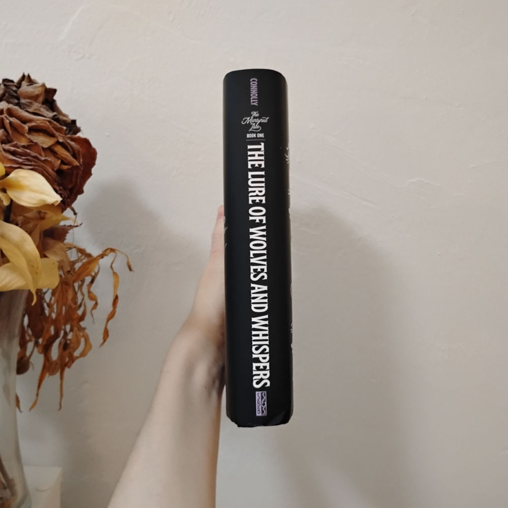 Photo of The Lure of Wolves and Whispers by Amanda Connolly spine which has black background and white text for the title, purple text for the author and publisher.